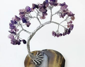 Könnte beinhalten: Eine dekorative Baumskulptur mit einem silbernen Drahtstamm und Ästen, verziert mit lila Amethyst-Edelsteinblättern. Der Baum ist auf einem polierten, oval geformten Achat-Sockel mit braunen, weißen und grauen Bändern montiert.