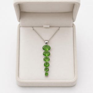 Close up of oval cut green gemstone set in 925 sterling silver vertical pendant, elegant peridot style necklace for women.
