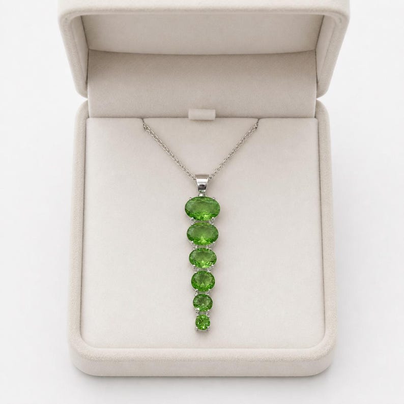 Close up of oval cut green gemstone set in 925 sterling silver vertical pendant, elegant peridot style necklace for women.
