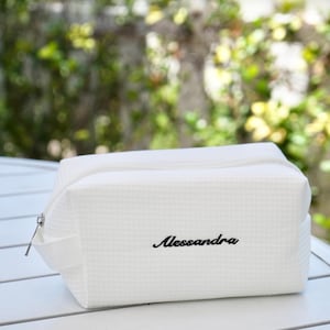 May include: White rectangular cosmetic bag with a textured waffle weave pattern. The bag has a zipper closure and a small handle. The name "Alessandra" is embroidered in black script on the front.