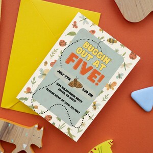 Könnte beinhalten: Eine Einladung mit dem Text "BUGGIN OUT AT FIVE!" zeigt eine Mottenillustration und Veranstaltungsdetails. Ein gelber Umschlag und ein Stift liegen neben der Einladung. Dekorative Holzformen und ein blaues Dreieck sind auf einer orangefarbenen Oberfläche verstreut.