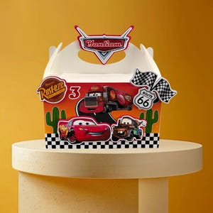 Puede incluir: Una caja blanca con personajes de la película Cars. La caja tiene un fondo rojo y naranja con imágenes de Rayo McQueen, Mate y otros personajes. La caja también tiene el texto "Yanliam", "3" y "Route 66".