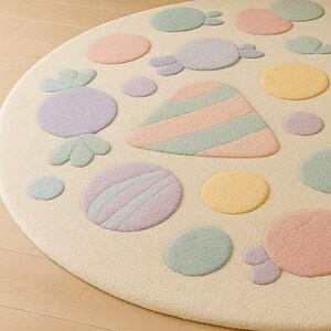 Puede incluir: Una alfombra redonda de color crema con dise&ntilde;os de caramelos y lunares en tonos pastel. La alfombra presenta varias formas en rosa, morado, amarillo y verde. La alfombra est&aacute; hecha de un material suave y afelpado, perfecta para la habitaci&oacute;n de un ni&ntilde;o o sala de juegos.