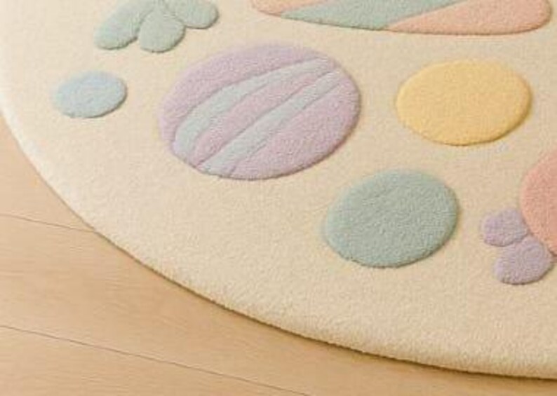 Puede incluir: Primer plano de una alfombra redonda de color crema con formas en colores pastel. La alfombra presenta c&iacute;rculos y dise&ntilde;os en forma de p&eacute;talos en tonos rosa, amarillo, verde y azul. La alfombra est&aacute; colocada sobre un suelo de madera clara.