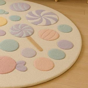 Puede incluir: Una alfombra redonda de color crema con un dise&ntilde;o de caramelos caprichoso. La alfombra presenta varias formas de caramelos de colores pastel, incluyendo piruletas, espirales y caramelos redondos. La alfombra est&aacute; hecha de un material suave y texturizado, perfecta para una habitaci&oacute;n infantil o sala de juegos.