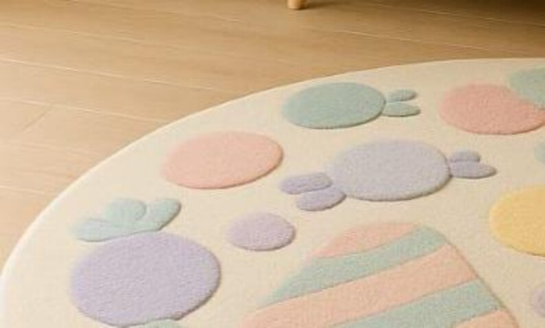 Puede incluir: Una alfombra redonda de color crema con caramelos y formas de colores pastel. La alfombra presenta dise&ntilde;os en azul claro, rosa, morado y amarillo. La alfombra est&aacute; hecha de un material suave y afelpado.