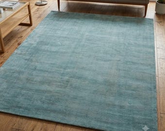 May include: A large, rectangular area rug in a solid, muted teal blue colour. The rug features a soft, uniform texture with subtle variations in tone across its surface, creating a consistent appearance that covers the wooden floor space.