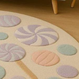 Puede incluir: Una alfombra redonda de color crema con dise&ntilde;os de caramelos y piruletas en tonos pastel. La alfombra presenta varias formas y colores, incluyendo lila claro, rosa, amarillo y verde, creando una est&eacute;tica juguetona y caprichosa. La alfombra est&aacute; hecha de un material suave y texturizado.