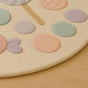 Puede incluir: Una alfombra redonda de color crema con un dise&ntilde;o caprichoso de caramelos. La alfombra presenta c&iacute;rculos de colores pastel y una forma de piruleta en rosa, lavanda y verde menta. La alfombra est&aacute; hecha de un material suave y texturizado.