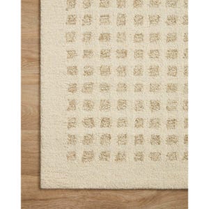 Könnte beinhalten: Cremefarbener Teppich mit einem sich wiederholenden Muster aus kleinen, erhabenen Quadraten in einem helleren Beigeton. Die Textur des Teppichs ist sichtbar, was auf ein weiches, gewebtes Material hindeutet. Der Rand des Teppichs ist sichtbar.