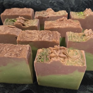 May include: A selection of handmade soaps, each with a two-tone colour scheme. The lower section is light green, and the upper is pinkish-brown. Some soaps feature decorative tops with green glitter.