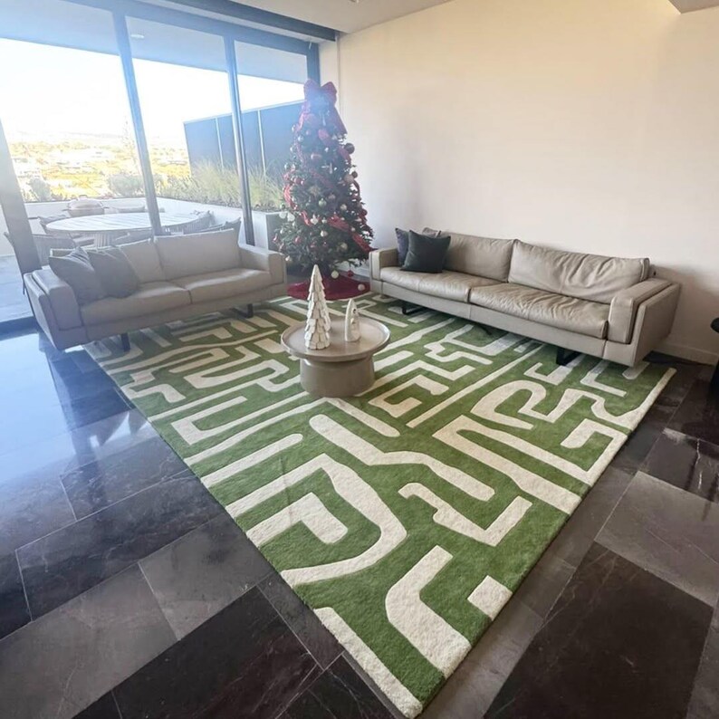 Puede incluir: Una alfombra grande con un patr&oacute;n geom&eacute;trico de laberinto en verde vibrante y crema. La alfombra est&aacute; situada en una habitaci&oacute;n con dos sof&aacute;s de cuero beige, una mesa de centro redonda con dos &aacute;rboles decorativos blancos y un &aacute;rbol de Navidad.