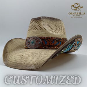 May include: A straw cowboy hat with a distressed finish. The hat features a decorative leather band with turquoise and silver accents. The brim is also decorated with turquoise and blue designs. The word "CUSTOMIZED" is displayed at the bottom.
