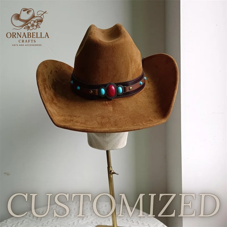 May include: A brown suede cowboy hat with a decorative band featuring turquoise and red stones. The hat is displayed on a mannequin head. The word "CUSTOMIZED" is at the bottom of the image. The logo "ORNABELLA CRAFTS HATS AND ACCESSORIES" is in the upper left corner.