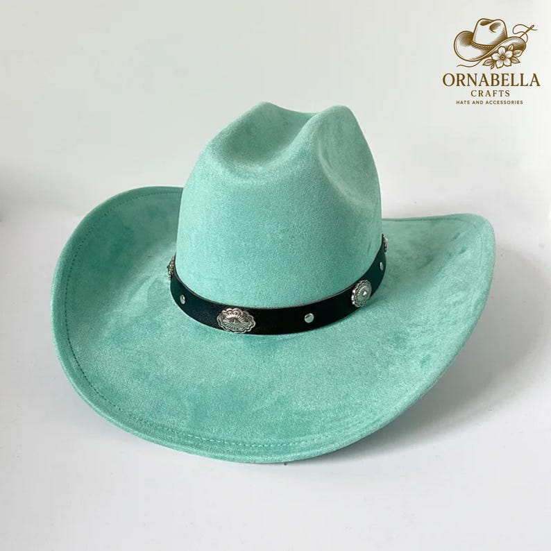 May include: A turquoise cowboy hat with a black band adorned with silver-colored decorative elements. The hat has a wide brim and a classic western design. The hat is made of a soft, suede-like material.