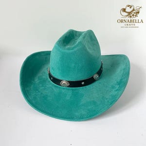 May include: A turquoise cowboy hat with a black band adorned with silver-colored embellishments. The hat has a wide brim and a classic western design. The hat is made of a soft material.
