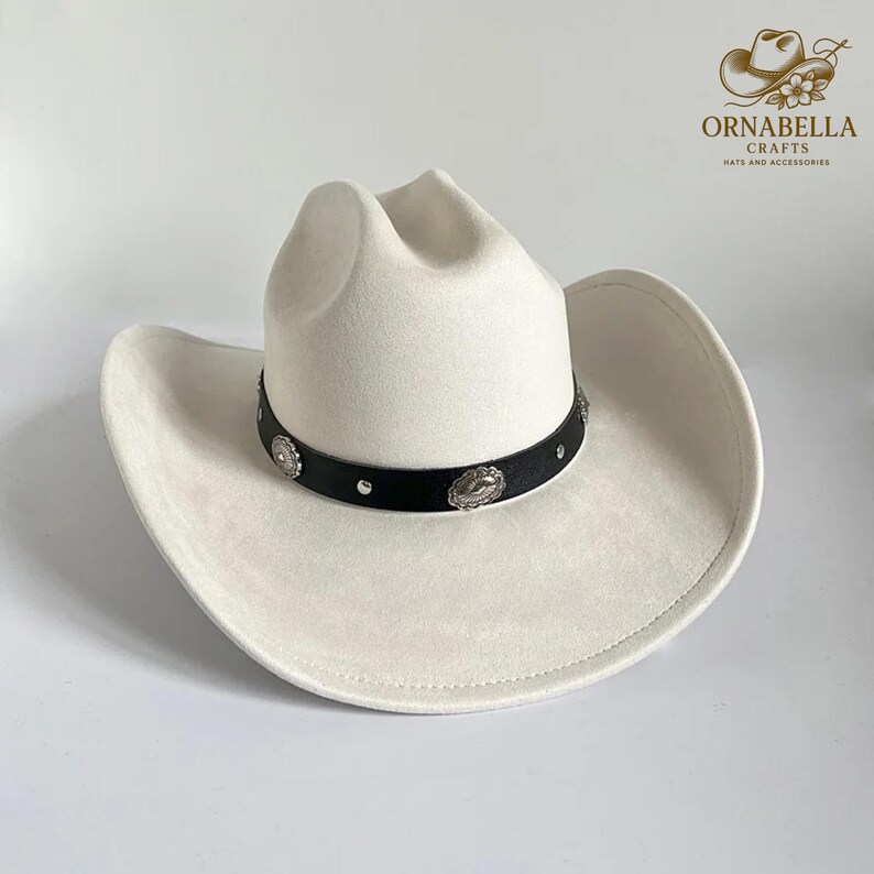 May include: A cream-colored cowboy hat with a black band adorned with silver-toned embellishments. The hat has a classic western design with a wide brim and a creased crown. The hat is a stylish accessory.