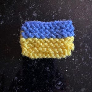 Pode incluir: Uma pequena bandeira ucraniana de malha. A bandeira é azul e amarela, com a faixa azul no topo e a faixa amarela na parte inferior.