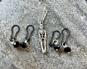 May include: Three pairs of silver skeleton earrings with black beads. The earrings are on a gray background.