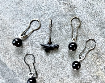 May include: Five black bead stitch markers with silver metal loops. The markers are shaped like small balls and are attached to the loops with a silver metal ring.