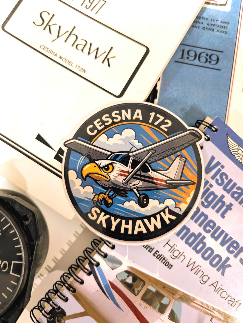 May include: A collection of aviation-themed items, including a Cessna 172 Skyhawk sticker with an eagle mascot, a notebook, and manuals. The sticker features a cartoon airplane design with the text "Cessna 172 Skyhawk."