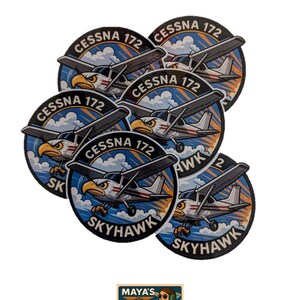 May include: A collection of circular stickers featuring a Cessna 172 Skyhawk airplane design. The stickers have a blue and white background with an eagle graphic. The text "Cessna 172" and "Skyhawk" are also included. A smaller sticker with the text "Maya's Hangar" is also present.