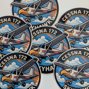 May include: A collection of round stickers featuring a Cessna 172 Skyhawk airplane with an eagle head design. The stickers have a blue and orange sky background with the text "CESSNA 172 SKYHAWK".