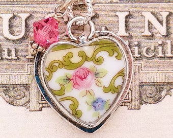 Peut inclure: Un collier avec un pendentif en forme de cœur argenté contenant un motif floral vintage. Le pendentif est orné d'un charme en cristal rose.