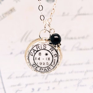 May include: A silver necklace with a round pendant featuring a white porcelain disc with black lettering that reads "PARIS R.P. 8* 14.IX 1925 DEPART". The pendant is accented with a black bead.