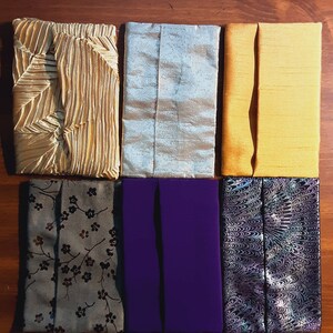 May include: Six fabric-covered items in various colors and patterns. The top row includes gold pleated, silver, and yellow fabrics. The bottom row features gray floral, purple, and black and white swirled designs. All items have a rectangular shape.