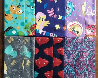 May include: A selection of folded fabric items with various patterns. Designs include cartoon characters, butterflies, sharks, and paisley. The colour scheme is diverse, with shades of blue, purple, red, and grey.