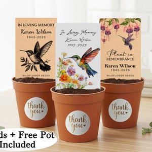 Op de afbeelding: Drie terracotta potten met wilde bloemzaden, elk met een herdenkingskaart. De kaarten tonen illustraties van kolibries en de tekst "In Loving Memory" en "Plant in Remembrance" met een naam en data. Elke pot heeft een "thank you" sticker.