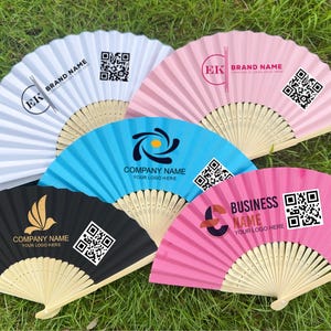 May include: A collection of open hand fans in various colors, including white, pink, blue, and black. Each fan features a unique logo and text, along with a QR code. The fans are made of paper and bamboo.