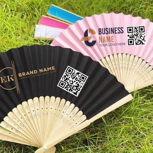 Könnte beinhalten: Eine Sammlung offener Papierfächer in verschiedenen Farben, darunter Schwarz und Rosa, mit Bambusgriffen. Der schwarze Fächer zeigt ein goldenes Logo und den Text "BRAND NAME" sowie einen QR-Code. Der rosa Fächer hat den Text "BUSINESS NAME" und einen QR-Code.