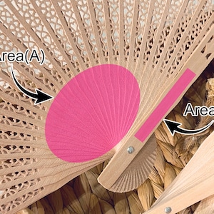 May include: A close-up of a partially open wooden hand fan with a pink center. The fan has a delicate, openwork design with floral patterns. The pink section is a solid color, contrasting with the natural wood tone.