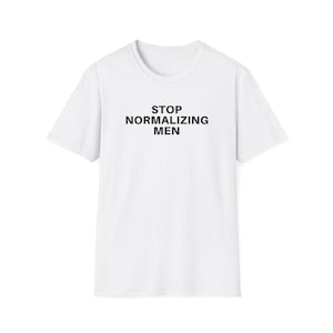 Pode incluir: Uma t-shirt branca com o texto preto "STOP NORMALIZING MEN". A t-shirt tem gola redonda e mangas curtas. O texto está centrado na frente da peça.