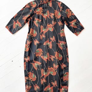 May include: A black silk cheongsam dress with a mandarin collar and a butterfly print. The dress has a red trim and is knee-length.