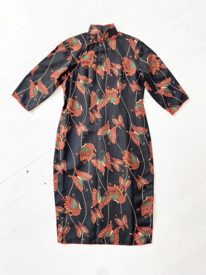 May include: A black silk cheongsam dress with a mandarin collar and a butterfly print. The dress has a red trim and is knee-length.