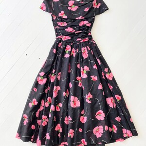 Peut inclure: Une robe &agrave; fleurs noire et rose avec un corsage pliss&eacute; et une jupe ample. La robe a des manches courtes et un col rond.