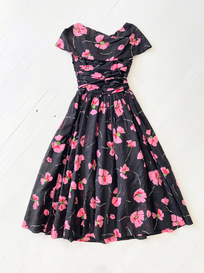 Peut inclure: Une robe &agrave; fleurs noire et rose avec un corsage pliss&eacute; et une jupe ample. La robe a des manches courtes et un col rond.