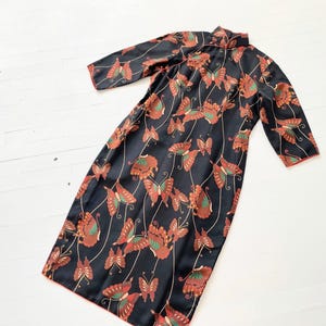 May include: A black dress with a mandarin collar and a butterfly print. The dress has 3/4 sleeves and a loose fit.