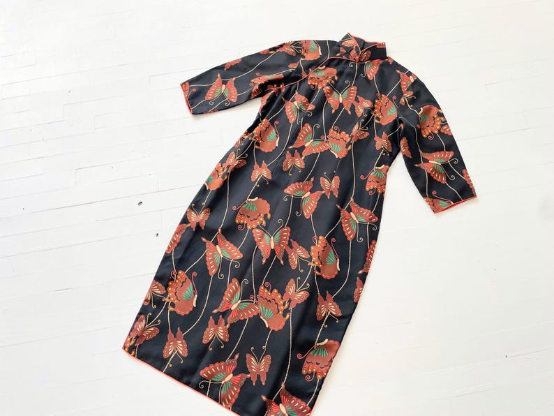 May include: A black dress with a mandarin collar and a butterfly print. The dress has 3/4 sleeves and a loose fit.
