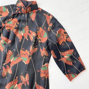 May include: A black silk dress with a mandarin collar and long sleeves. The dress is decorated with a pattern of red, green, and gold butterflies.