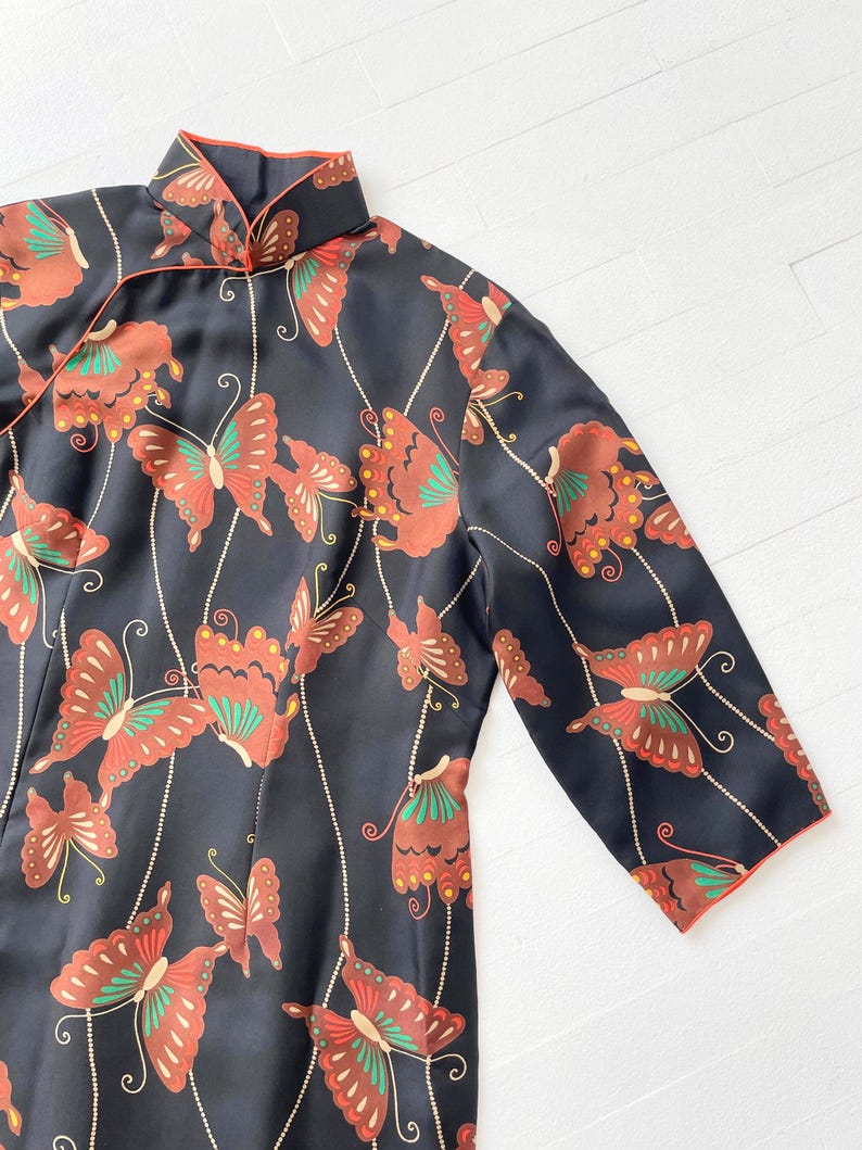 May include: A black silk dress with a mandarin collar and long sleeves. The dress is decorated with a pattern of red, green, and gold butterflies.