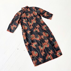 May include: A black dress with a mandarin collar and a butterfly print. The dress has a red trim and is made of a silky fabric.