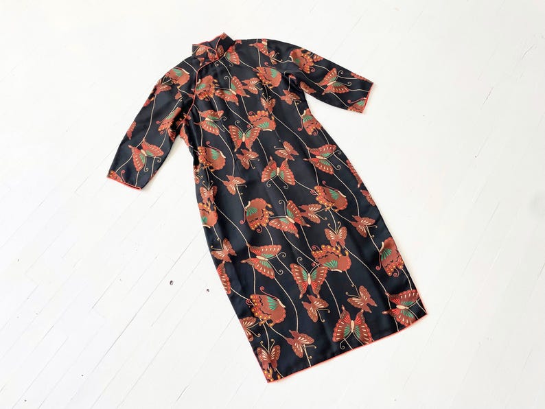 May include: A black dress with a mandarin collar and a butterfly print. The dress has a red trim and is made of a silky fabric.