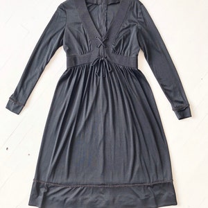 May include: A black long-sleeved dress with a lace-up neckline and a gathered skirt. The dress has a fitted bodice and a flowing skirt. The dress has a scalloped hem.