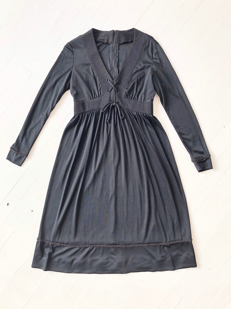 May include: A black long-sleeved dress with a lace-up neckline and a gathered skirt. The dress has a fitted bodice and a flowing skirt. The dress has a scalloped hem.