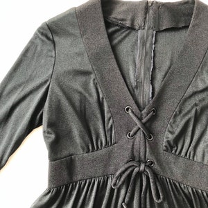May include: A black long-sleeved dress with a V-neck and a lace-up detail at the waist.