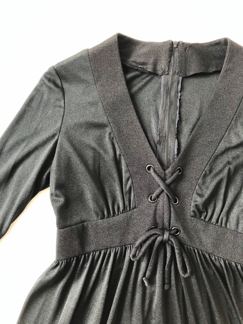 May include: A black long-sleeved dress with a V-neck and a lace-up detail at the waist.